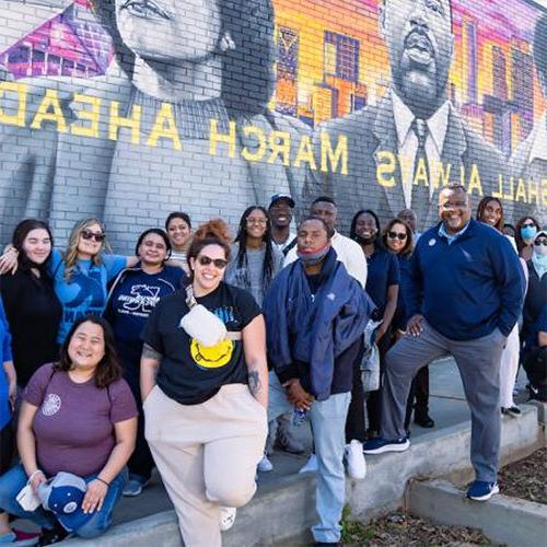 Group of people standing in front of a large mural featuring Martin Luther King Jr